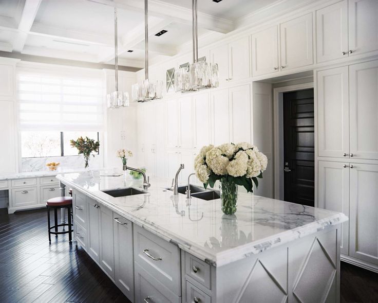 A beautiful white kitchen with dark flooring. The countertops are .