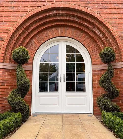White double doors with glass panels and spiral topiaries